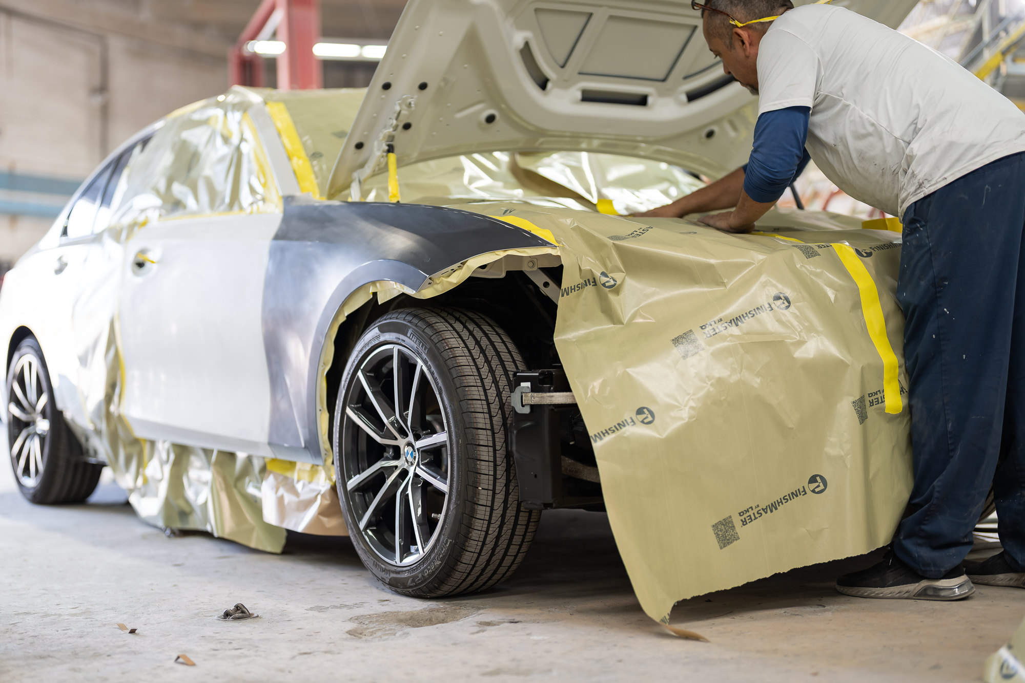 Technician carefully masking a BMW for paint work at Precision Paint & Body Miami