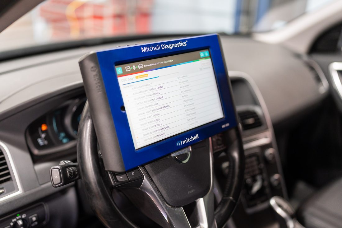 A diagnostics scan tool mounted on a vehicle steering wheel, running a module fault code scan