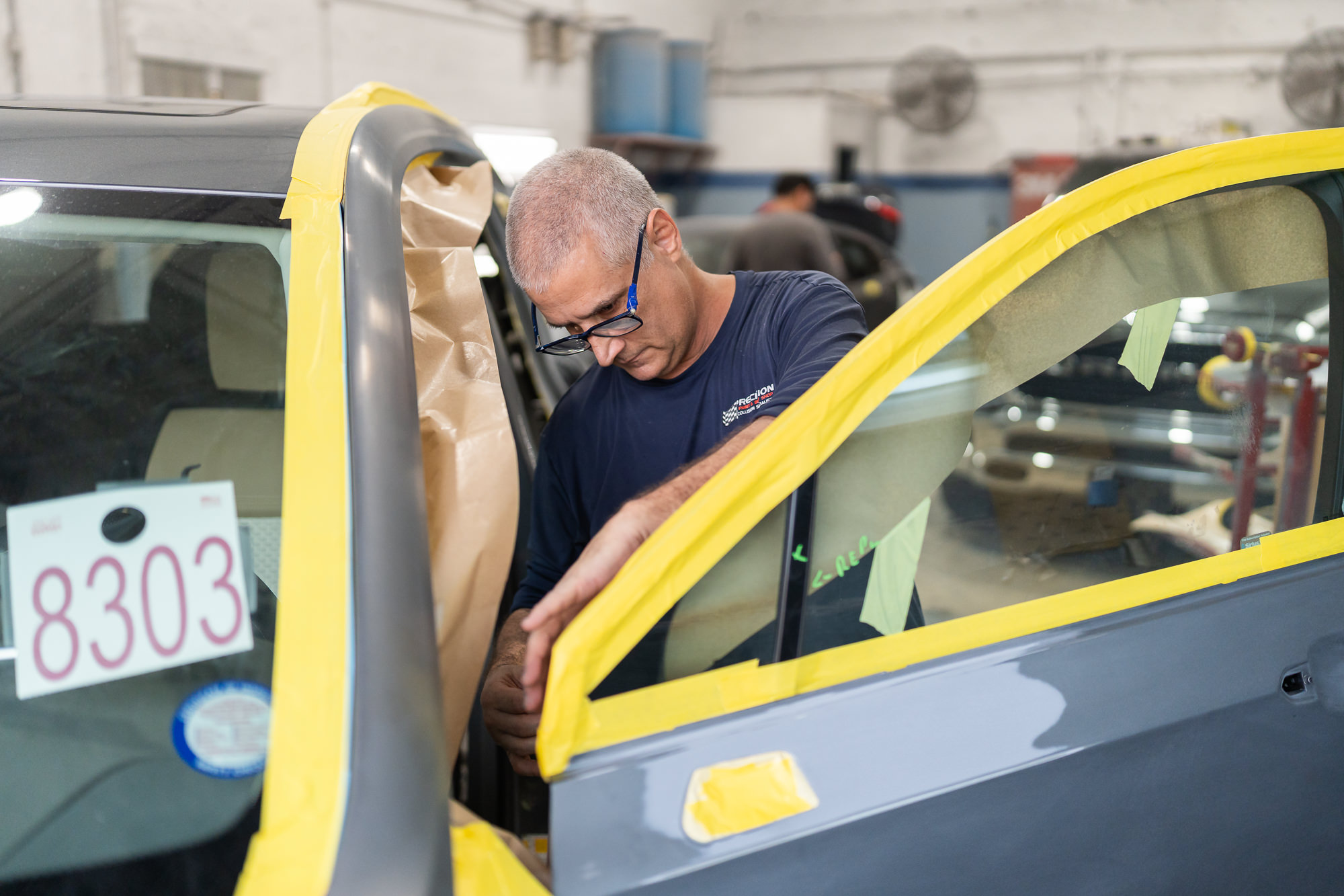 Technician carefully applying masking tape before fender paint repair in Miami auto body shop