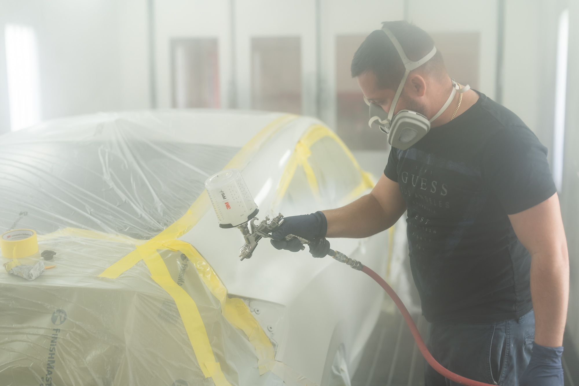 Precision painter applying automotive paint inside professional spray booth in Miami