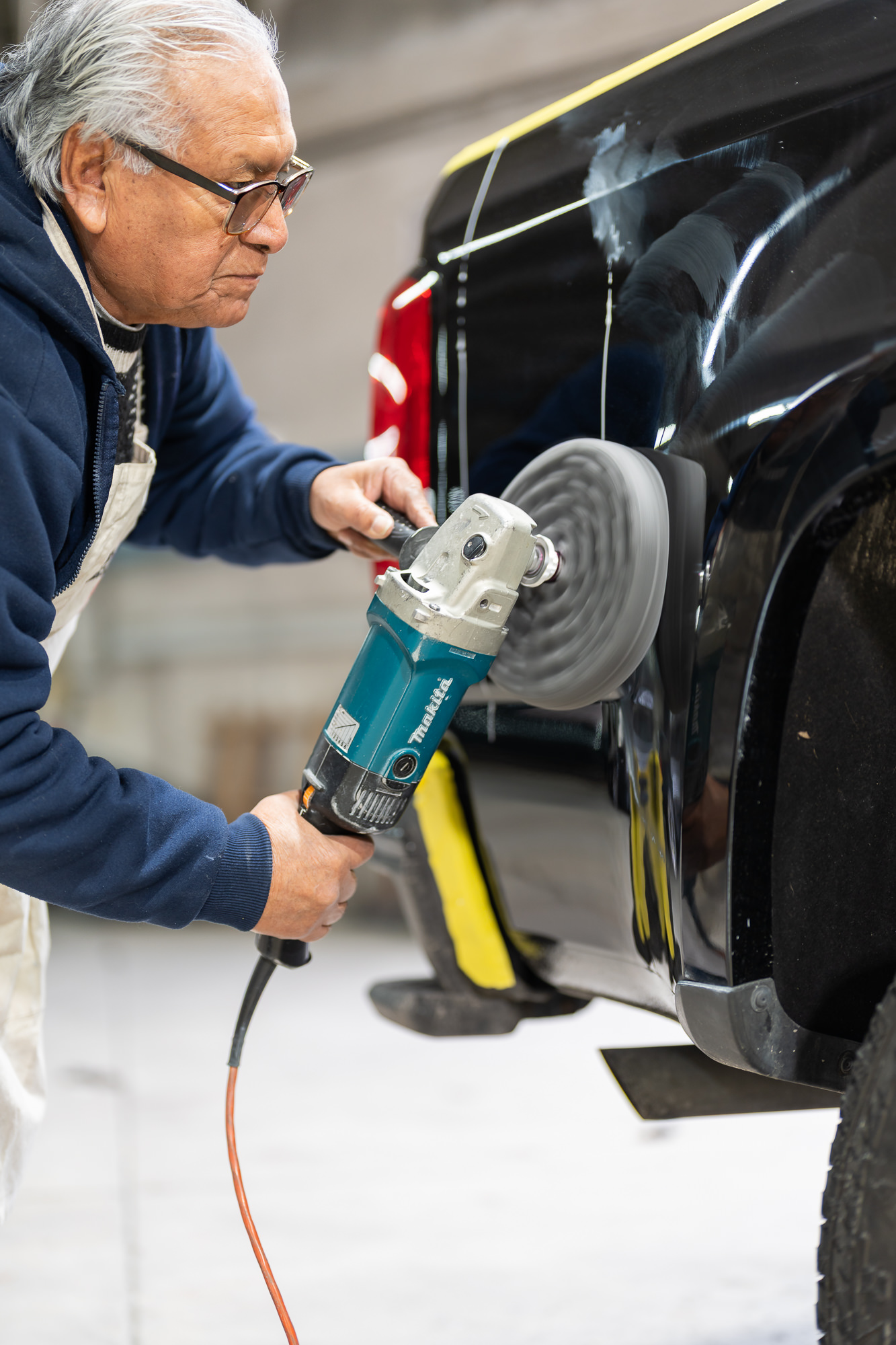 Auto body technician using rotary buffer for paintless dent repair on a vehicle door panel